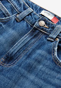 Jeans in denim blu con vita media, dotati di chiusura a cerniera, cuciture in rame e un’etichetta con la scritta "Barrel". Texture strappata vicino ai bordi.