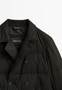 Cappotto antivento nero con design doppiopetto, caratterizzato da colletto a righe, chiusura a due bottoni e texture trapuntata. Etichetta edizione limitata visibile.