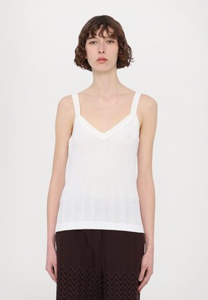 Camisole blanche avec une texture en chevron, larges bretelles et un décolleté en V, associée à un pantalon à motif zigzag foncé.