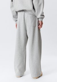 Grå joggingbukser lavet af blødt stof, med rummeligt snit, elastisk taljebånd og en firkantet baglomme. Glat tekstur, uden mønstre.