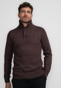 Suéter de punto marrón oscuro con cuello alto, puños acanalados y una tapeta de dos botones. Presenta un tejido texturizado y un corte relajado.