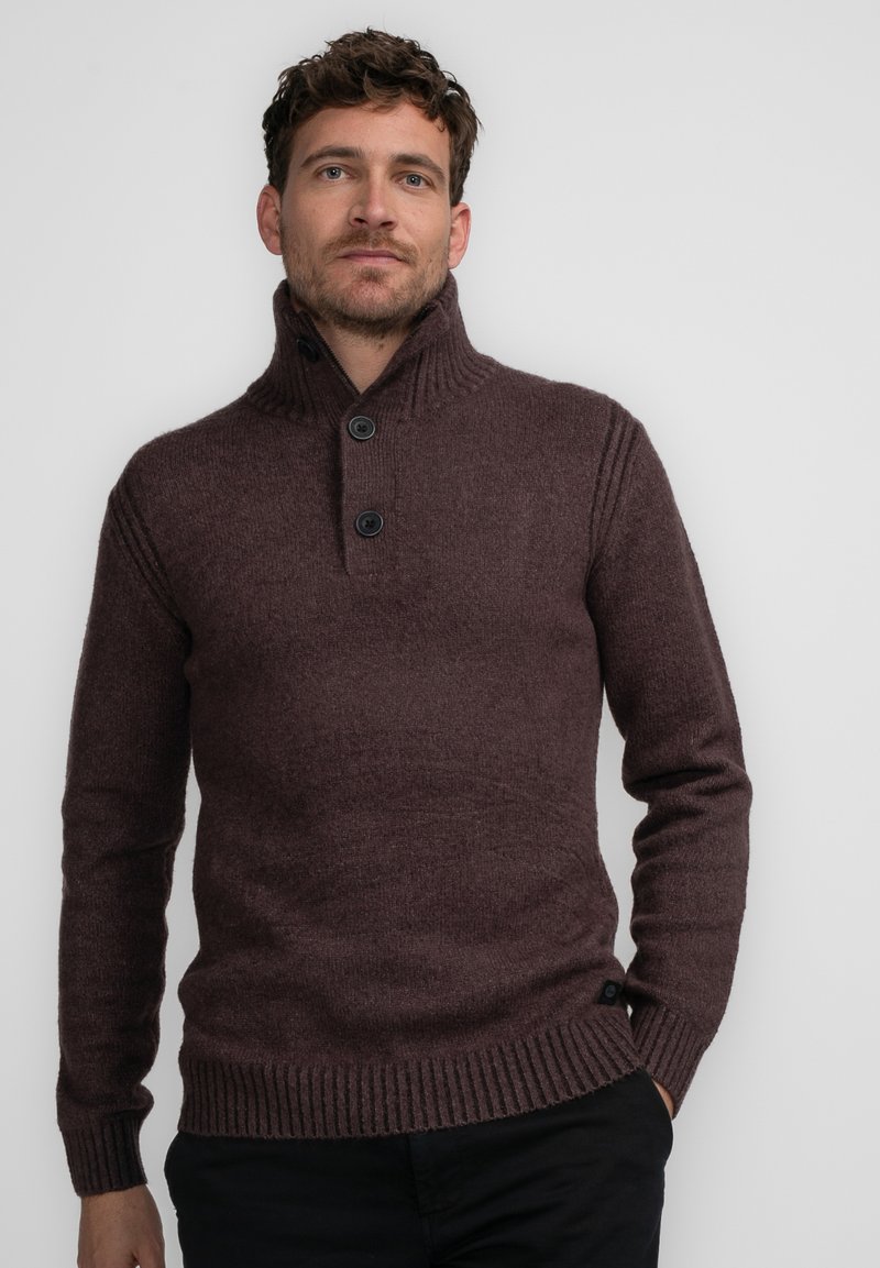Suéter de punto marrón oscuro con cuello alto, puños acanalados y una tapeta de dos botones. Presenta un tejido texturizado y un corte relajado.