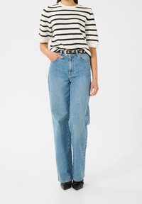 Pull à manches courtes rayé blanc et noir, jean en denim bleu à coupe décontractée, ceinture noire avec ferrures en argent, et chaussures noires à bouts pointus.