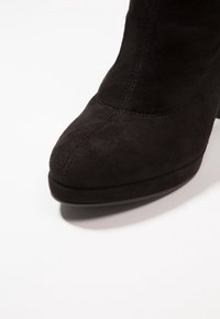 Černé nubukové kotníkové boty s kulatou špičkou, hladkým povrchem a jemným prošíváním na boku. Mají malý, pevný podpatek.