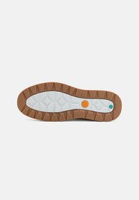 Gummi-Außensohle in Braun und Weiß, mit einem strukturierten Griffmuster und markiertem Logo. Sechseckige und kreuzförmige Designs verbessern die Traktion.