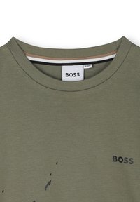 T-shirt verde oliva con scollatura a girocollo, leggero design a macchie nere e logo "BOSS" stampato sul lato sinistro. Materiale misto cotone.