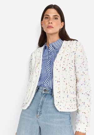 Giacca bianca con texture e macchie multicolori, dotata di scollo rotondo e frontale aperto. Abbinata a una camicia a righe blu e bianche.