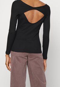 Top nero a maniche lunghe con design sulla schiena a torsione, caratterizzato da un'apertura sulla schiena e texture a coste. Abbinato a pantaloni a gamba larga di colore viola chiaro.