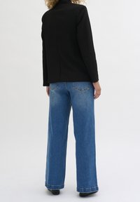 Czarna marynarka o dopasowanym kroju, zestawiona z szerokimi niebieskimi dżinsami o prostych nogawkach. Dżinsy mają jasne wykończenie i klasyczne tylne kieszenie.