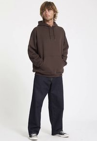 Bruine hoodie met een voorzak en trekkoorden, gecombineerd met donkerblauwe spijkerbroek en zwarte sneakers. Simpel, casual ontwerp.