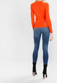 Jasnopomarańczowy sweter z prążkowanym wzorem i długimi rękawami, zestawiony z dopasowanymi niebieskimi dżinsami oraz czarnymi botkami na szpilce. Prosty design, bez wzorów.