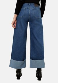 Jeans in denim blu a gamba larga con orlo sfrangiato e polsini in azzurro chiaro a contrasto, caratterizzati da un vita alta e tasche posteriori standard.