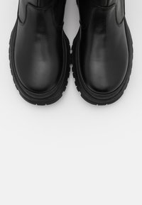 Svarta läderankelstövlar med en glansig finish, rund tå och tjock gummisula. Sömsdetaljer längs sidorna och ingen synlig hårdvara.