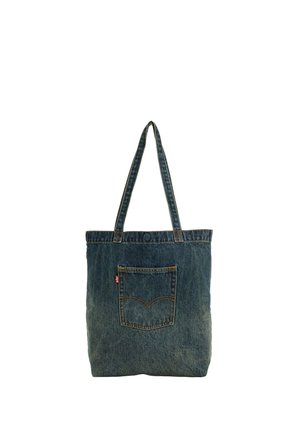 Denim-totepose med lange håndtag og en ydre lomme foran, med orange syning og en lille rød etiket på lommens side.