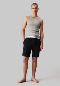 Grijze katoenen tanktop gecombineerd met zwarte shorts met een witte tailleband. Eenvoudig ontwerp, ontspannen pasvorm en geen patronen of accenten.