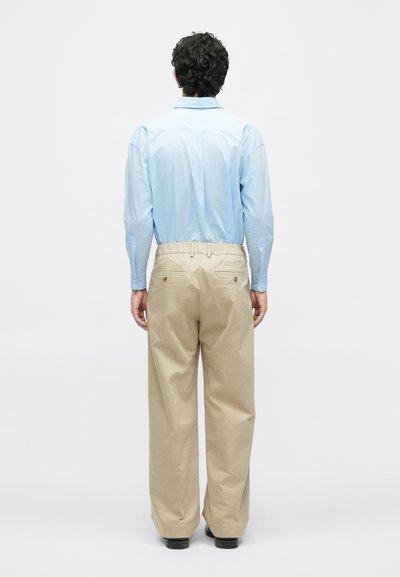 Šviesiai mėlyna ilgomis rankovėmis palaidinė derinama su laisvai krentančiomis smėlio spalvos kelnėmis. Kelnės turi dvi užpakalines kišenes su mygtukų uždarymu. Palaidi audinio tekstūra.