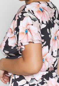 Sukienka w kwiatowy wzór z krótkimi falbaniastymi rękawami. Czarna baza z dużymi różowymi kwiatami i zielonymi liśćmi. Miękki materiał o gładkiej fakturze.