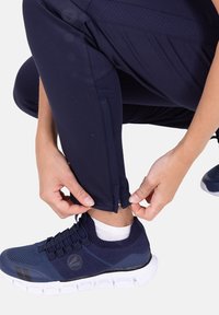 Marineblaue Sporthose mit Reißverschluss an den Beinenden, glatter Textur und atmungsaktivem Stoff, kombiniert mit dunkelblauen Turnschuhen und weißen Socken.