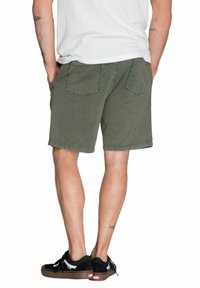 Olijfgroene shorts van katoen met een relaxte pasvorm, voorzien van twee achterzakken en een opgerolde zoom, gecombineerd met zwarte sneakers.