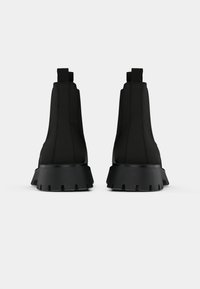 Svarte ankelsko med en glatt, teksturert overdel, elastiske sider og en kraftig gummisåle med et taggete mønster for grep.