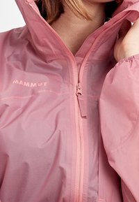 Lehká bunda s kapucí v jemně růžové barvě, vyrobená z hladkého, lesklého materiálu. Má přední zip a elastické manžety, s logem jako detailem.