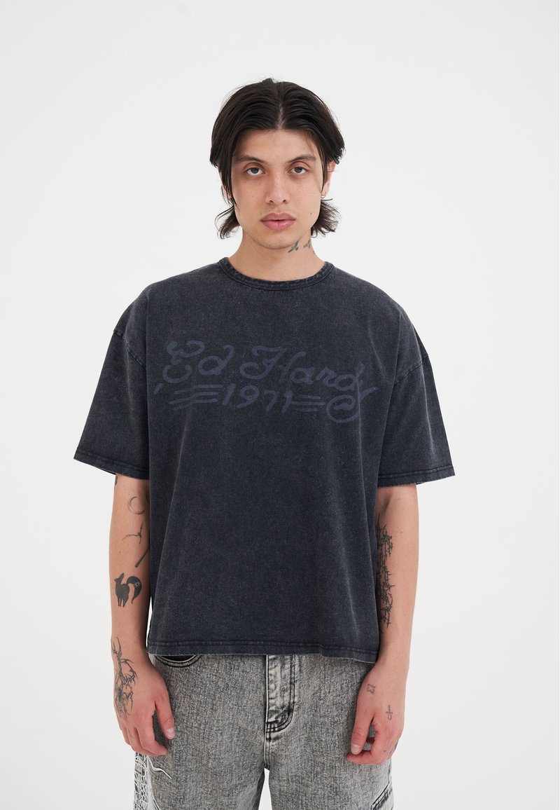 Sort denim oversized t-shirt med rund hals og korte ærmer, der har et falmet logo i mørkeblå.