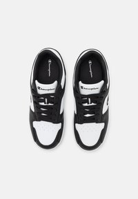 Chaussures de sport noir et blanc avec un dessus en cuir lisse, des blocs de couleur contrastés, des perforations sur le bout, et des lacets noirs plats.