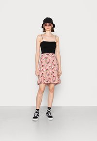 Top ajustado preto com alças finas, saia rodada rosa com flores e barra em franja, chapéu preto estilo balde e meias xadrez com ténis.