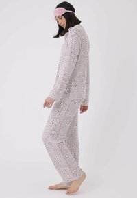 Tryckt pyjamasset i ljusrosa med svarta prickar, bestående av en knäppt skjorta och långa byxor, prydda med en sidostrip och ficka.