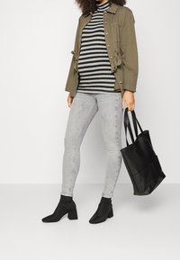 Chaqueta verde oliva, suéter de cuello alto a rayas grises, jeans ajustados gris claro, botas de tobillo negras con tacón y un bolso negro.