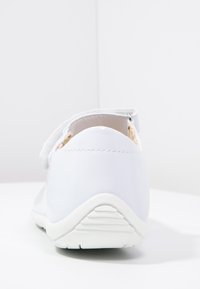 Witte synthetische schoen met een ronde vorm, textuurzool en verstelbare band. De achterkant heeft een soepele afwerking en subtiele stiksel details.