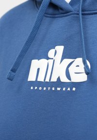 Μπλε φούτερ με κουκούλα από απαλό ύφασμα, με μεγάλο λευκό λογότυπο "nike" και κείμενο "SPORTSWEAR" από κάτω. Διαθέτει κουκούλα με κορδόνι.