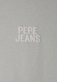 Svetlo sivý textil s ryhovanou textúrou, na ktorom sa v strede výrazne vyšíva biele logo "PEPE JEANS".