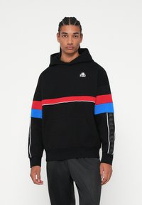 Felpa nera con strisce orizzontali rosse e blu, piping bianco e logo Kappa. Presenta una tasca a marsupio e un motivo testurizzato sulle maniche.
