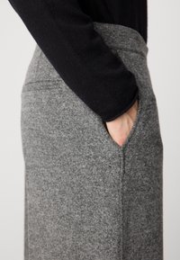 Grijze, patroonrokken met een getailleerd ontwerp. Heeft een tailleband en zijzakken. Zachte textuur zichtbaar in de stofdetails.