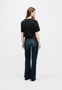 Μαύρη βαμβακερή μπλούζα με κοντά μανίκια, σε συνδυασμό με σκούρο μπλε καμπάνες τζιν που διαθέτουν κλασικό σχέδιο με πέντε τσέπες και διακριτικές λεπτομέρειες ραφής.