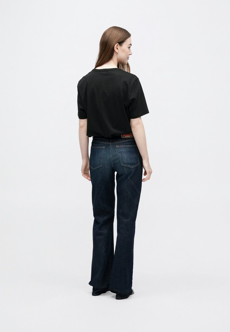 Camiseta negra de algodón de manga corta, combinada con vaqueros azul oscuro acampanados que presentan un diseño clásico de cinco bolsillos y detalles sutiles de costura.