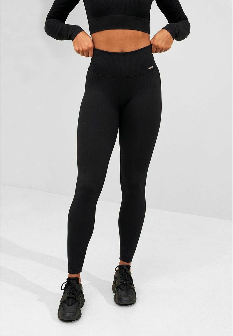Black ribbed leggings with a high waistband, fitted design, and stretchy fabric, paired with black athletic shoes.