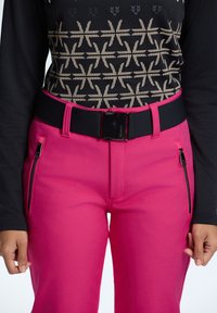 Pink pants with a fitted design, featuring two side zippers, paired with a long-sleeve top that has a black and gold geometric pattern. Black belt included.