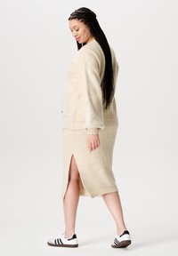 Beige wollen mix trui en midi rok met een zijsplit. Chunky brei textuur en zakken in de trui. Schoenen zijn zwart-witte sneakers.
