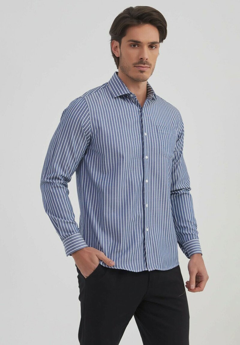 Chemise à rayures bleu et blanche à manches longues avec un col boutonné, une poche frontale et une texture lisse. Associée à un pantalon de couleur sombre.