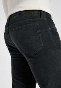 Jeans in velluto a coste neri con una finitura texturizzata, caratterizzati da un classico design a cinque tasche e un patch in pelle sul retro della vita.