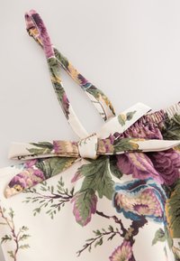 Stoff mit Blumenmuster mit grünen, violetten und blauen Blättern und Blumen, mit einer gebundenen Schleife und dünnem verstellbarem Schultergurt.