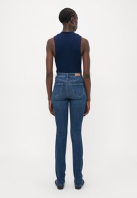 Marineblå ermeløs topp, høy midje blå jeans, tettsittende straight-leg design, lys utvanning, to baklommer, og en brun merkeskilt på midjebåndet.