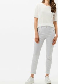 Camiseta blanca ligera combinada con pantalones grises claros con patrón y bolsillos con cremallera, de corte ajustado, completada con zapatillas blancas.