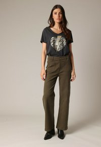 T-shirt noir à manches courtes avec imprimé cœur en éclairs dorés, associé à un pantalon large taille haute vert olive et des bottines noires.