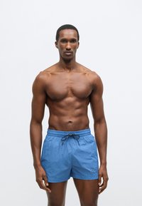 Μπλε μαγιό σορτς από ελαφρύ ύφασμα, με ελαστική μέση και κορδόνι, καθώς και κεντημένη λεπτομέρεια λογότυπου στο πλάι.