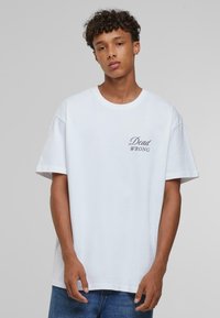 Hvid bomulds-T-shirt med korte ærmer og rund halsudskæring, prydet med sort trykt tekst "Dead WRONG" på venstre side. Glat tekstur.