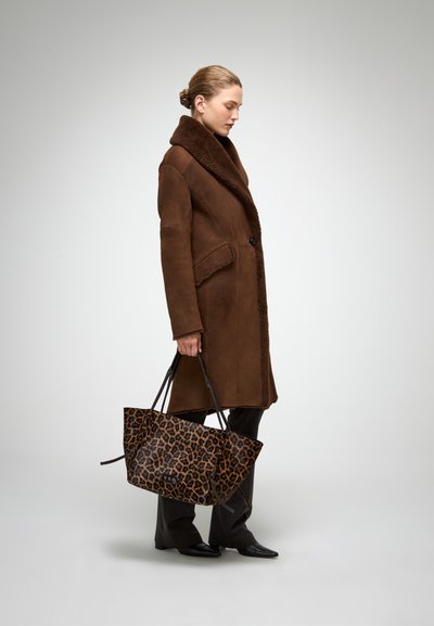 Brūns aitu kažoks ar plašu apkakli, pogu aizdari un kabatām, apvienots ar leoparda raksta somu un melniem šauriem biksēm.