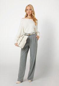 Pantaloni grigi chiari su misura, maglione oversize bianco in maglia, borsa neutra con dettagli, e tacchi a punta nudi. Tessuto morbido e vestibilità rilassata.
